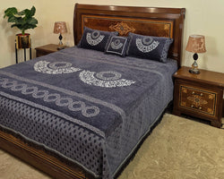 Bed with blue patterned cover and wooden headboard in a bedroom setting.