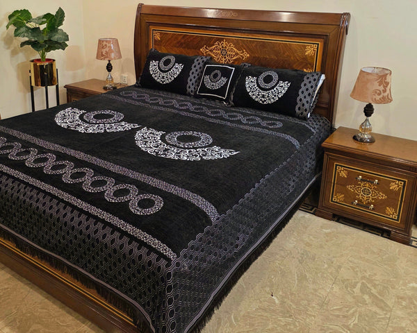 Black embroidered bedspread on a wooden bed with matching pillows in a bedroom setting.