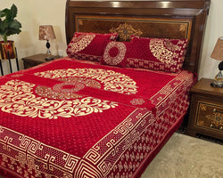 Red and gold patterned bedspread on a wooden bed with matching pillows in a bedroom setting.
