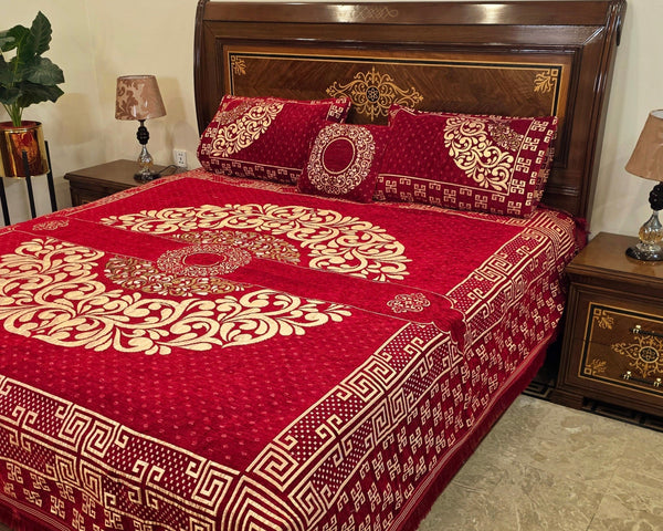 Red and gold patterned bedspread on a wooden bed with matching pillows in a bedroom setting.