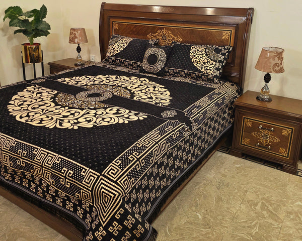 Decorative black and gold bedspread on a bed with matching pillows in a bedroom setting.