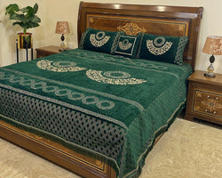 Decorative green bedspread with intricate patterns on a wooden bed in a bedroom setting.
