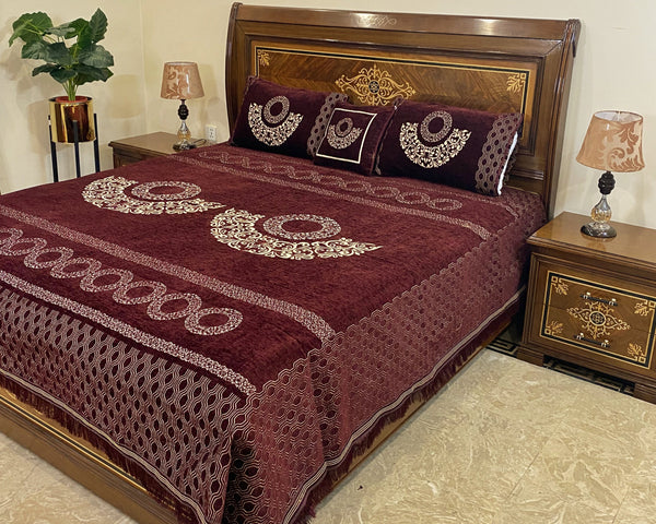 Bed with maroon embroidered cover and pillows in a bedroom setting.