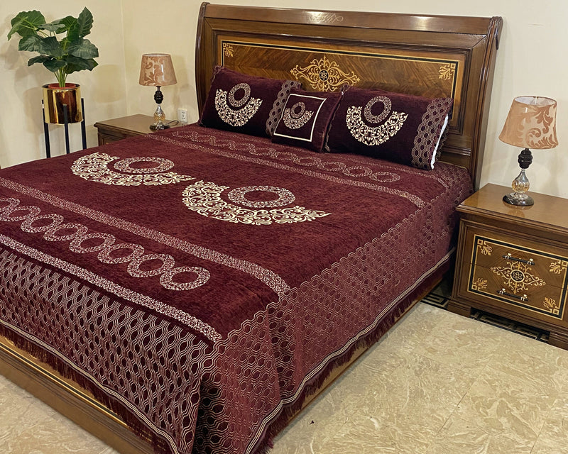 Bed with maroon embroidered cover and pillows in a bedroom setting.